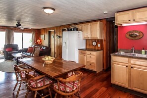 A kitchen with wooden cabinets, a dining table with chairs, a refrigerator, and a clock on the wall. - Bluegill Hill Hutchins Lake, Wineries, Breweries! (Fennville)