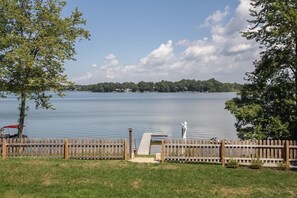 A lakeside view with a wooden dock, grassy area, and a distant shoreline with trees and buildings. - Bluegill Hill Hutchins Lake, Wineries, Breweries! (Fennville)