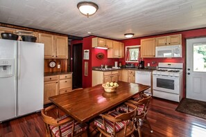 Una cocina con armarios de madera, un refrigerador blanco, una mesa de comedor de madera con sillas y una pared roja.