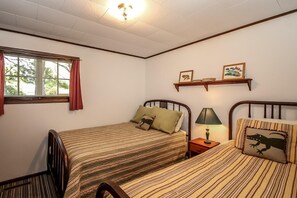A bedroom with two beds, a nightstand, a lamp, a window with curtains, and wall-mounted shelves with pictures. - Bluegill Hill Hutchins Lake, Wineries, Breweries! (Fennville)