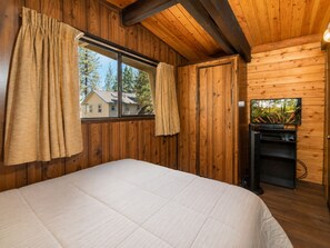 Une pièce avec un lit, une fenêtre avec des rideaux et un téléviseur fixé à un mur en bois.
