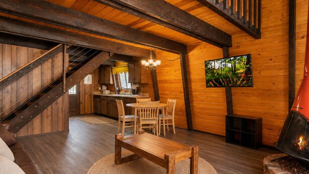A cozy cabin interior with a wooden staircase, a dining area, a fireplace, and a kitchen. - Fanciful Winter's Lake - Portable AC, Walk to Lake, Close to Village, Fireplace, Barbecue (Big Bear Lake)