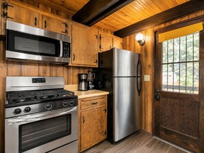 A kitchen with wooden cabinets, stainless steel appliances, a stove, oven, microwave, and refrigerator. - Fanciful Winter's Lake - Portable AC, Walk to Lake, Close to Village, Fireplace, Barbecue (Big Bear Lake)