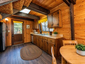 A wooden interior with a kitchen, dining area, and a large window. - Fanciful Winter's Lake - Portable AC, Walk to Lake, Close to Village, Fireplace, Barbecue (Big Bear Lake)