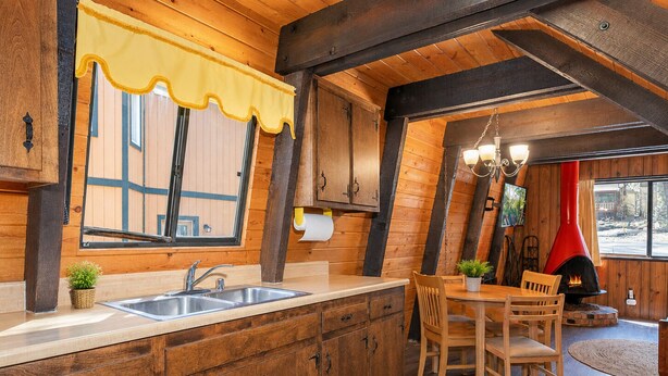 A rustic kitchen with wooden cabinets, a sink, and a dining area with chairs and a table.