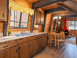 A rustic kitchen with wooden cabinets, a sink, and a dining area with chairs and a table. - Fanciful Winter's Lake - Portable AC, Walk to Lake, Close to Village, Fireplace, Barbecue (Big Bear Lake)