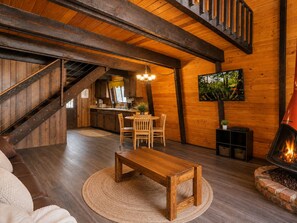 Un intérieur chaleureux avec un escalier en bois, un coin repas doté d’une table ronde et une cheminée.