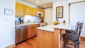 A kitchen with wooden cabinets, a microwave, a coffee maker, and a fruit bowl on the counter. - Kapaa Shore Ocean & Pool View Condo (Kapaa)