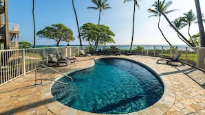 A pool area with lounge chairs and palm trees, overlooking a body of water. - Kapaa Shore Ocean & Pool View Condo (Kapaa)