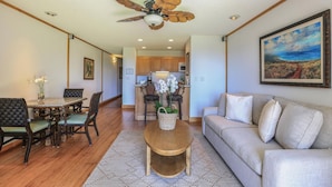 A spacious living area with a dining table, chairs, a sofa, a ceiling fan, and a kitchen in the background. - Kapaa Shore Ocean & Pool View Condo (Kapaa)