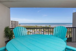 Enjoy the ocean view from this balcony with a table and chairs, surrounded by a railing and a potted plant.