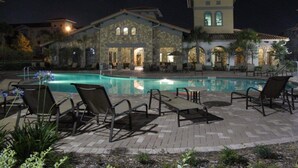 Vista nocturna de un área de piscina con sillas de descanso y un edificio de piedra con ventanas arqueadas.