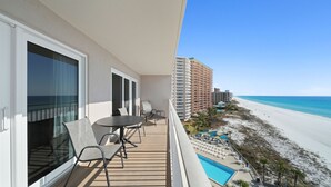 A balcony with a table and chairs, overlooking a beach and a hotel building. - D804 3 pools - Awesome View of the Beach! (Panama City Beach)