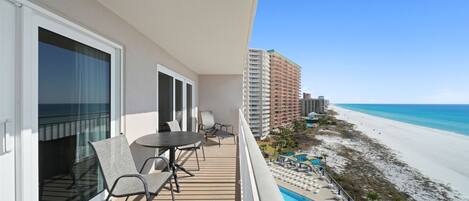 Un balcón con una mesa y sillas, con vista a una playa y un edificio de hotel.