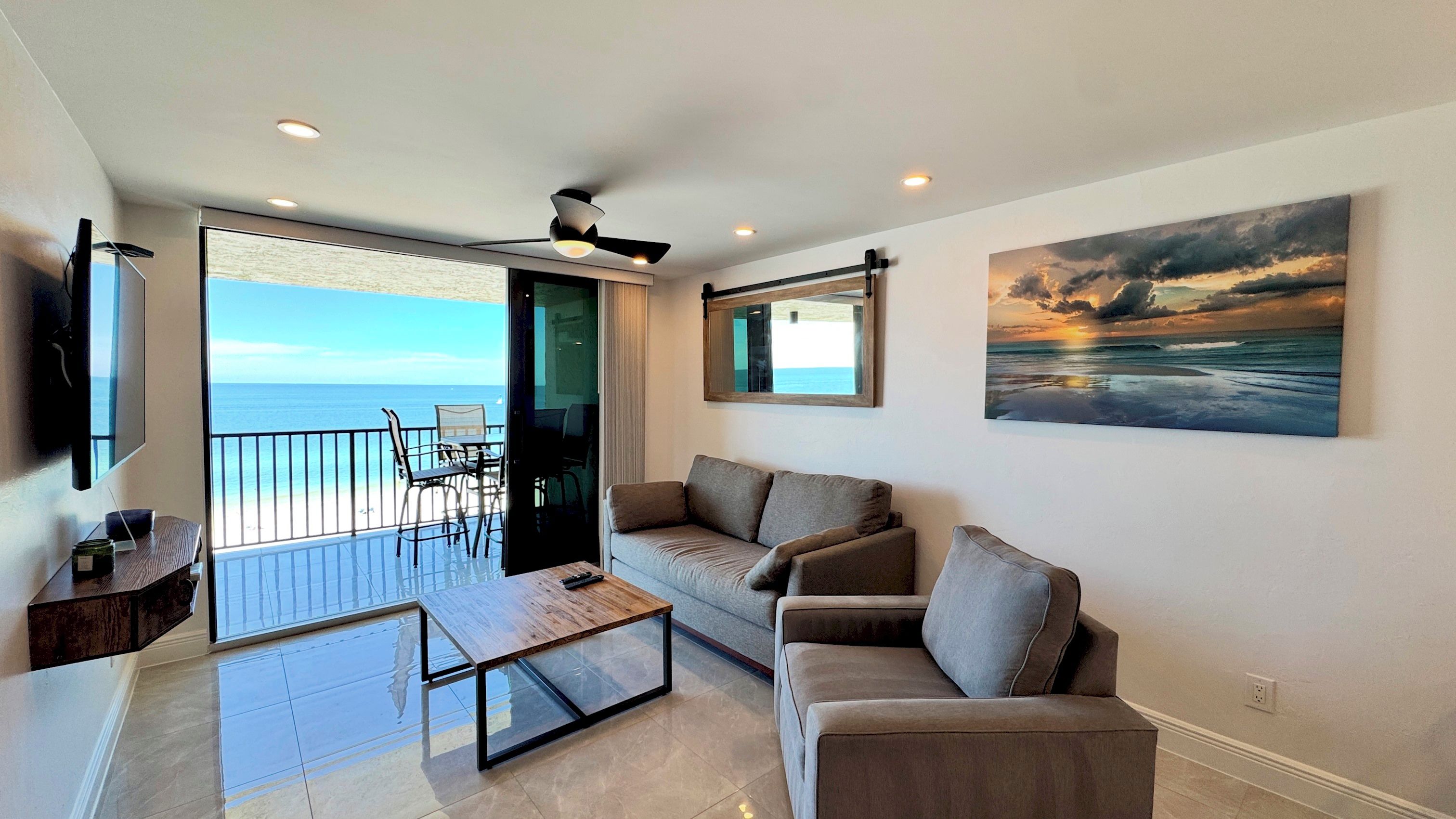 A modern living room with a sofa, coffee table, and a painting of a sunset over the ocean.