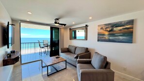 A modern living room with a sofa, coffee table, and a painting of a sunset over the ocean. - Sea Winds 603: Totally Remodeled Beach Front Condo! (Marco Island)