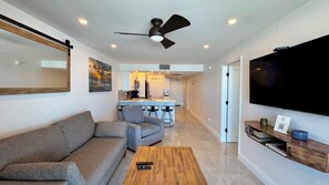 A modern living room with a sofa, a coffee table, a TV mounted on the wall, and a ceiling fan. - Sea Winds 603: Totally Remodeled Beach Front Condo! (Marco Island)