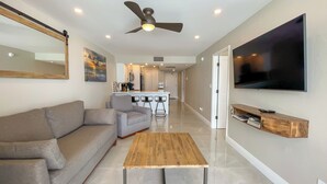 A modern living room with a sofa, a coffee table, a TV, and a kitchen area in the background.
