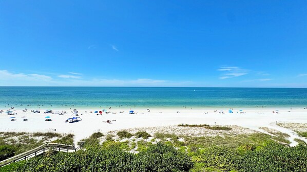 A beach with a wooden walkway leading to the shore, clear skies, and a calm sea. - Sea Winds 603: Totally Remodeled Beach Front Condo! (Marco Island)