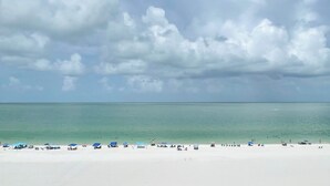 A beach with clear turquoise water, white sand, and a few umbrellas and beach chairs.