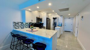 A modern kitchen with a marble countertop, bar stools, and stainless steel appliances. - Sea Winds 603: Totally Remodeled Beach Front Condo! (Marco Island)