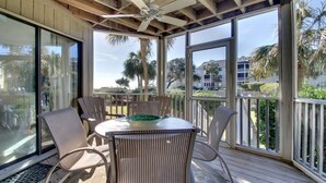 A covered outdoor area with a table and chairs, large windows, and a ceiling fan. - 102 E Port O Call by AvantStay | Beachfront + Ocean Views + Communal Pool (Isle of Palms)