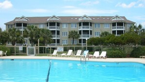 A swimming pool with lounge chairs and a multi-story building in the background. - 102 E Port O Call by AvantStay | Beachfront + Ocean Views + Communal Pool (Isle of Palms)