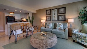 A living room with a sofa, chairs, a coffee table, and artwork on the wall. - 102 E Port O Call by AvantStay | Beachfront + Ocean Views + Communal Pool (Isle of Palms)