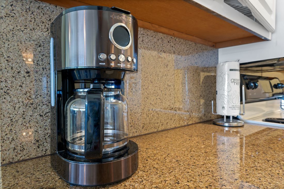 Eine Kaffeemaschine aus Edelstahl mit einem Glasbehälter auf einer Granit Arbeitsplatte.