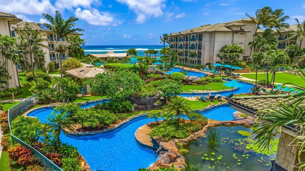 A resort with multiple swimming pools surrounded by lush greenery and palm trees, overlooking a beach.