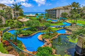 Ein Resort mit mehreren Schwimmbecken, umgeben von üppiger Vegetation und Palmen, mit Blick auf einen Strand.