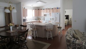 A modern kitchen with wooden cabinets, a central island, and a dining area with a table and chairs. - POLO RIDGE NICE RANCH CLOSE TO DINING SHOPPING BANKS AND MORE THE VILLAGES FL (The Villages)