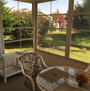 A conservatory with a glass roof, a round table, a cushioned chair, and a wooden bench.