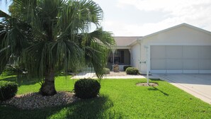A single-story house with a garage, a well-maintained lawn, and a palm tree. - POLO RIDGE NICE RANCH CLOSE TO DINING SHOPPING BANKS AND MORE THE VILLAGES FL (The Villages)