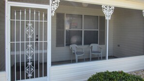 A single-story house with a covered porch, a sliding glass door with decorative metal bars, and two white plastic chairs on the porch. - POLO RIDGE NICE RANCH CLOSE TO DINING SHOPPING BANKS AND MORE THE VILLAGES FL (The Villages)