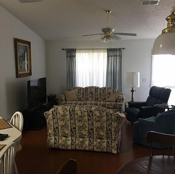 A living room with a sofa, a chair, a television, and a ceiling fan.