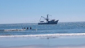 Une plage avec un bateau de pêche sur l’eau et des personnes au loin.