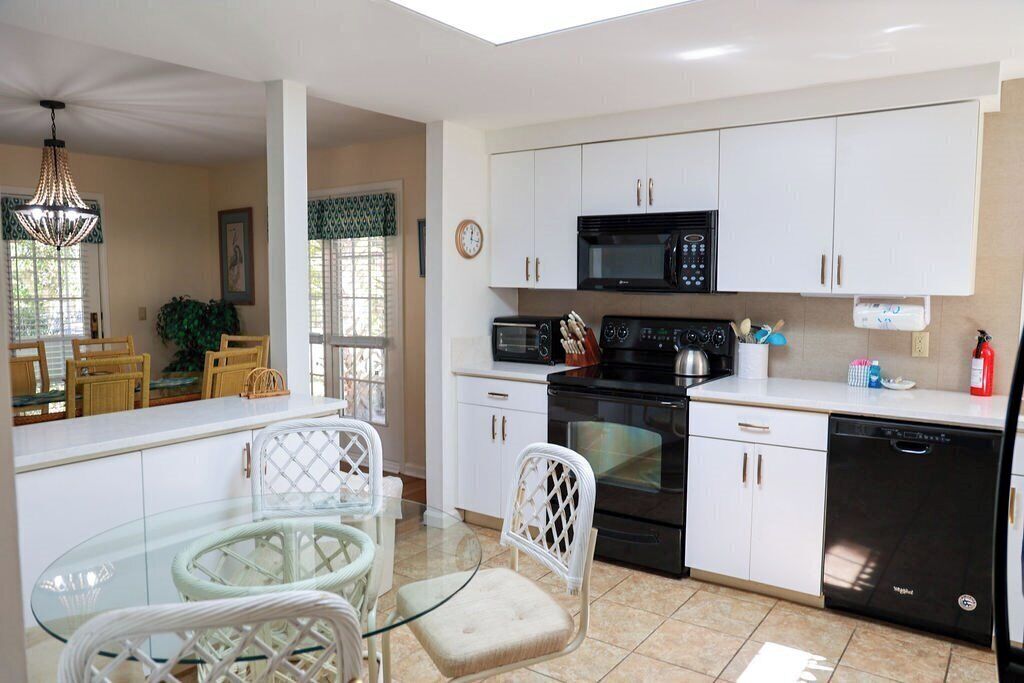 A modern kitchen with white cabinets, a black microwave, and a dishwasher. There is a glass dining table with chairs.