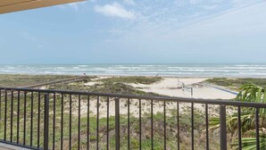 Blick auf den Strand von einem Balkon mit Geländer, feiner Sand und Meer.