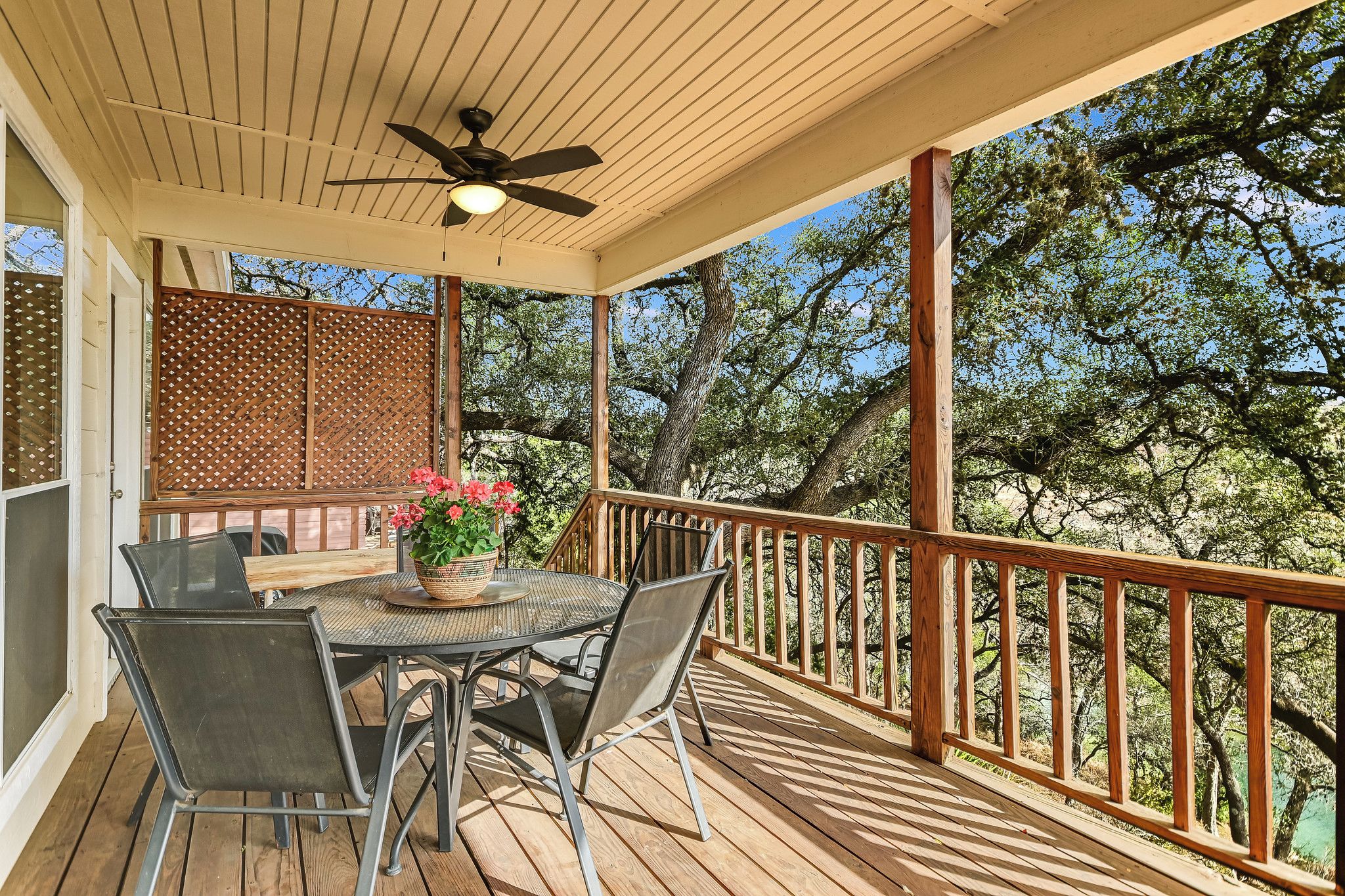 A covered outdoor deck with a table and chairs, a ceiling fan, and a view of trees.