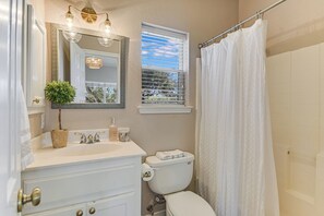 A bathroom with a white sink, a mirror, a toilet, a shower curtain, and a window with blinds. - Beautiful views and the Crystal Clear waters of the Blanco River await you! (Wimberley)