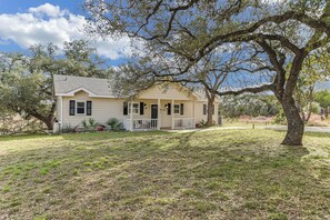 A single-story house with a porch, surrounded by grass and trees. - Beautiful views and the Crystal Clear waters of the Blanco River await you! (Wimberley)