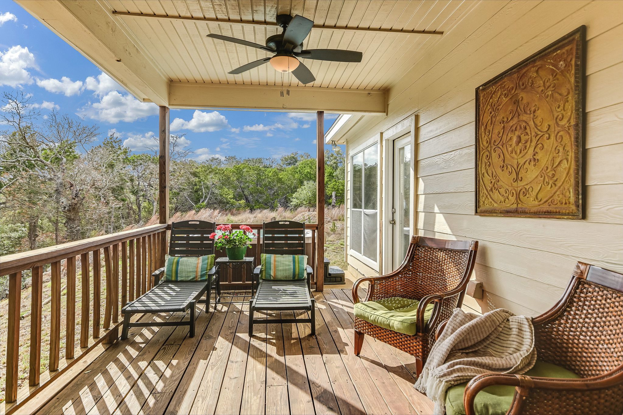 A wooden deck with a ceiling fan, wicker furniture, and a view of trees.