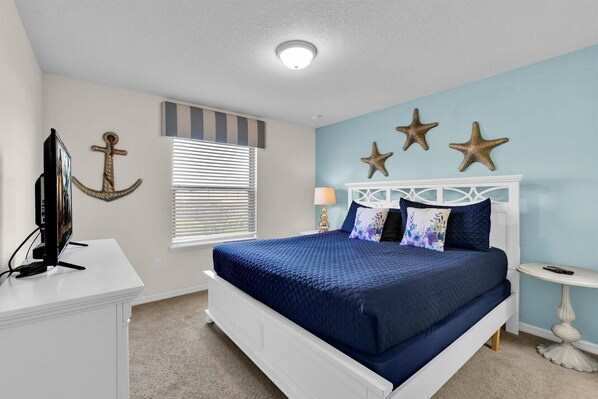 A bedroom with a bed, a television, a window with blinds, and decorative starfish on the wall.