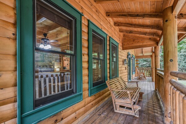 Sit on the porch and enjoy the view of the surrounding trees from this cabin's outdoor space.