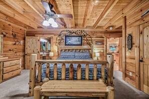 Cozy cabin-style room with a central bed, ceiling fan, and warm wooden accents.