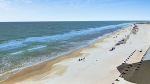A beach with a long stretch of sand, a few umbrellas, and people. - 1403 Ocean Club by AvantStay | Beach Home w/ Great Kitchen  + Easy Beach Access (Isle of Palms)