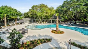 A swimming pool with lounge chairs and umbrellas, surrounded by trees and a covered seating area. - 1403 Ocean Club by AvantStay | Beach Home w/ Great Kitchen  + Easy Beach Access (Isle of Palms)