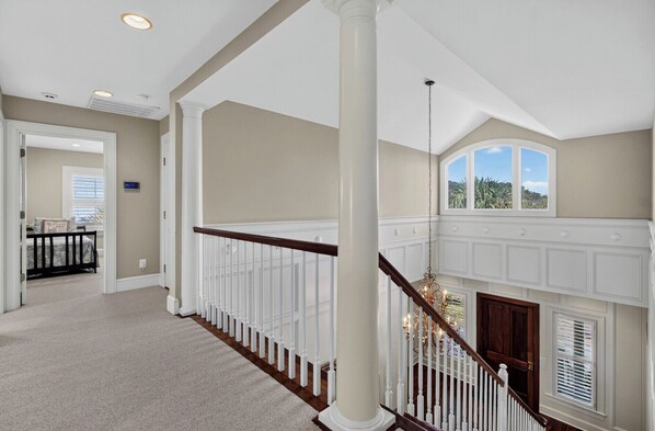 Un intérieur spacieux avec un plafond haut, un magnifique escalier et une vue dégagée par une grande baie vitrée.