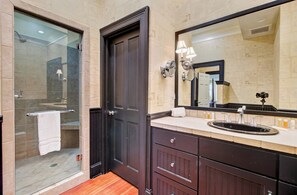 A modern bathroom with a glass shower enclosure, a dark wooden door, a large mirror, and a vanity with a sink.